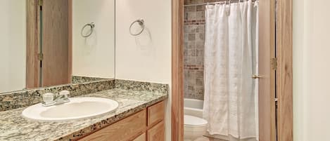Un baño con lavamanos de encimera de granito, armarios de madera, inodoro y cortina de ducha.