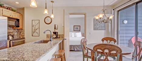 A modern kitchen with granite countertops, wooden stools, and pendant lighting.