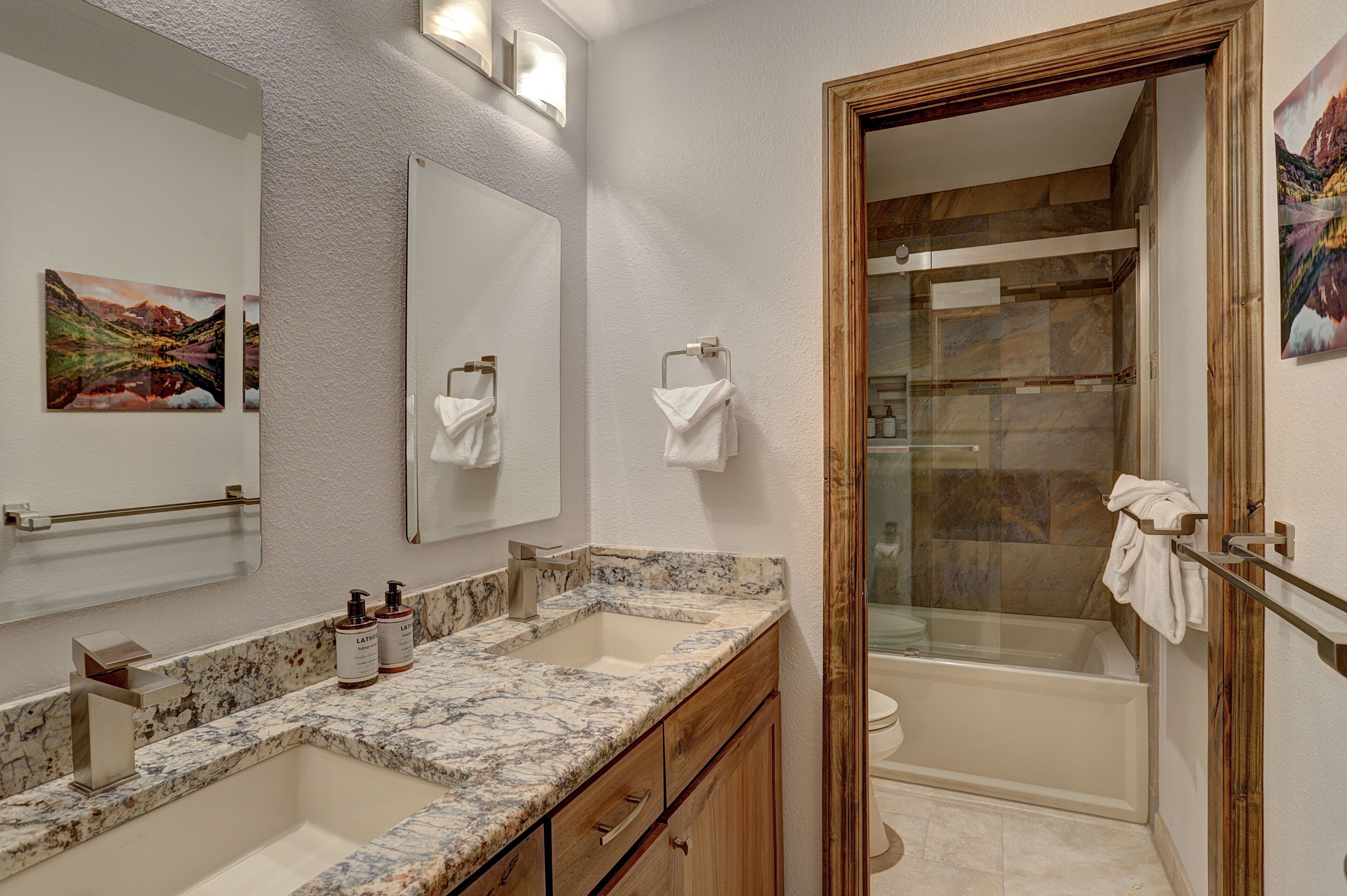 A bathroom with a marble countertop, a sink, a mirror, and a shower area.