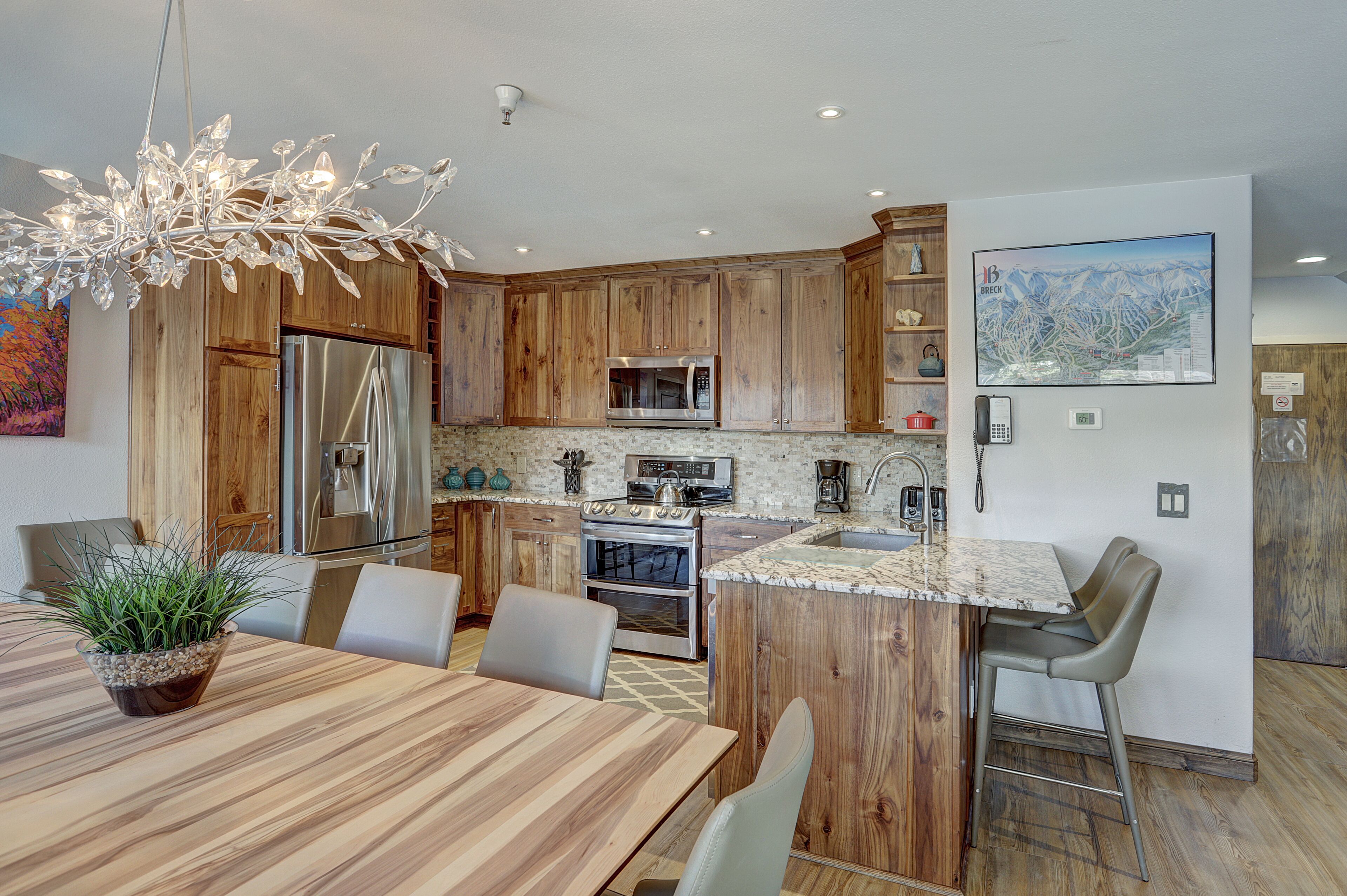 A modern kitchen with wooden cabinets, stainless steel appliances, a marble countertop, and a dining area with a wooden table and chairs.