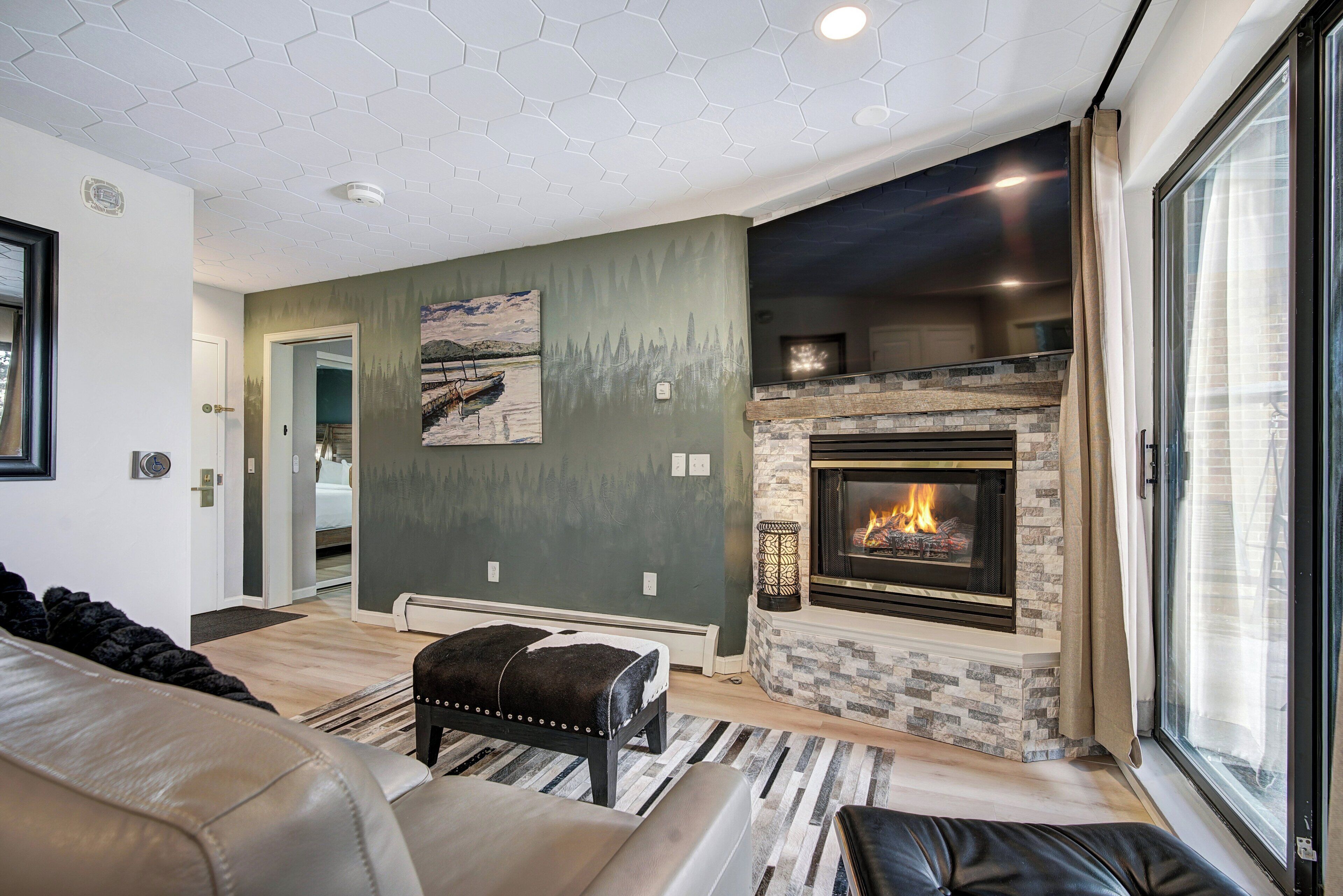 A living room with a fireplace, a sofa, a bench, and a view through a large window.