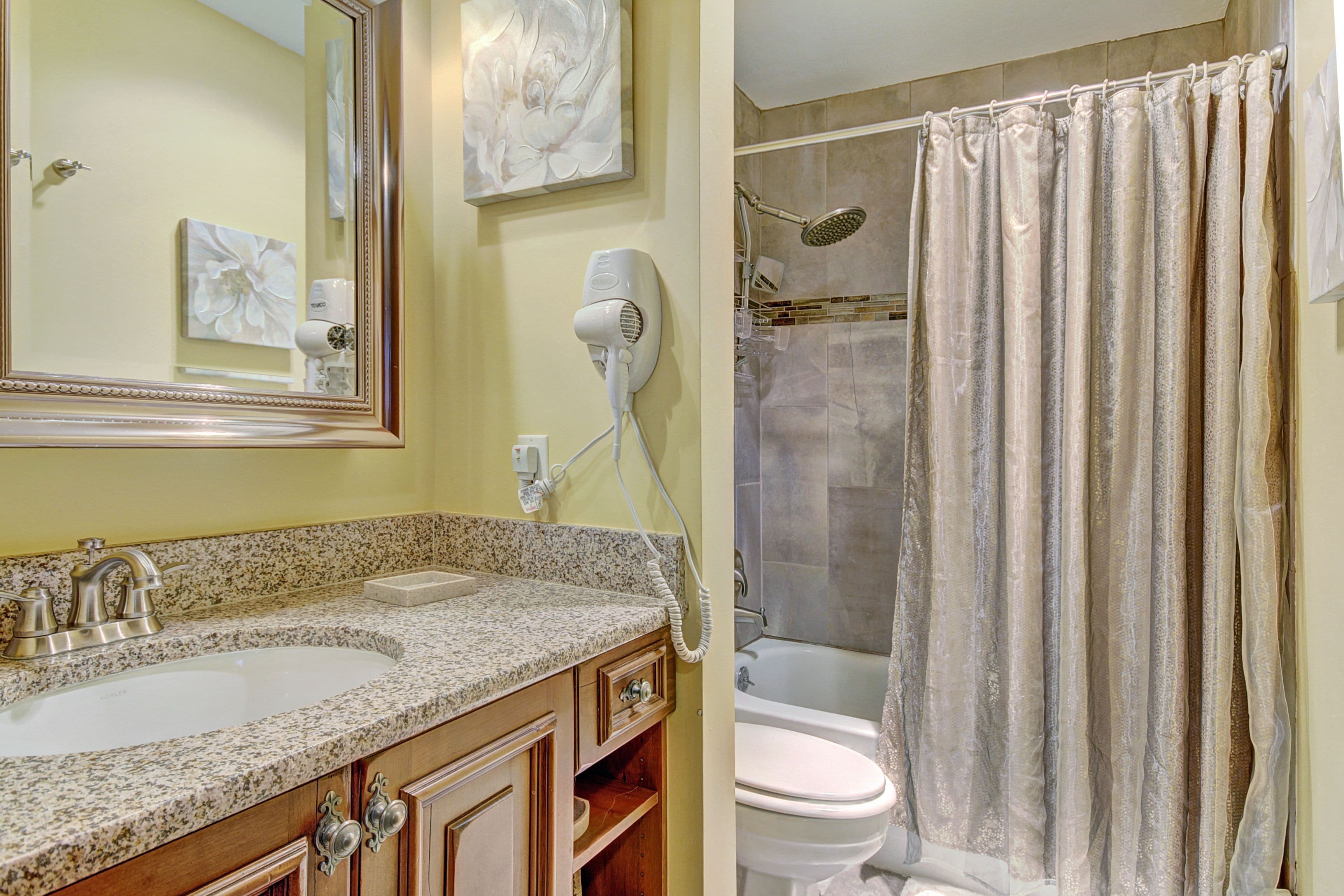 A bathroom with a granite countertop sink, a mirror, a hairdryer, and a shower curtain.