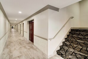 Un pasillo de hotel con suelo de mármol, una puerta de madera y una escalera con diseño.