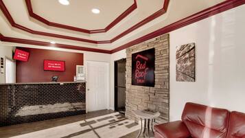 Un hall de hotel con una mesa de recepción, un letrero de Red Roof Inn, un sofá de cuero y una chimenea.