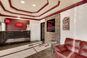 A hotel lobby with a reception desk, a Red Roof Inn sign, a leather sofa, and a fireplace. - Red Roof Inn & Suites Pensacola - NAS Corry (Pensacola)