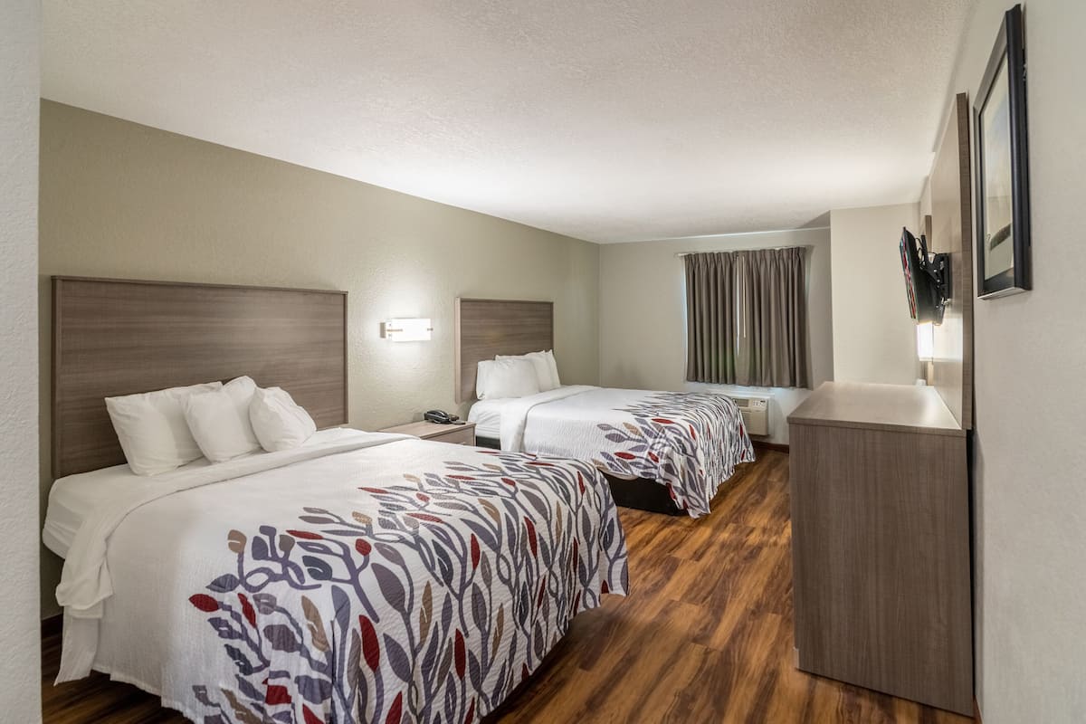 Habitación de hotel con dos camas, piso de madera, un escritorio y televisión fijada en la pared.