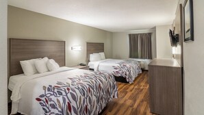 Een hotelkamer met twee bedden, een houten vloer, een bureau en een raam met gordijnen.