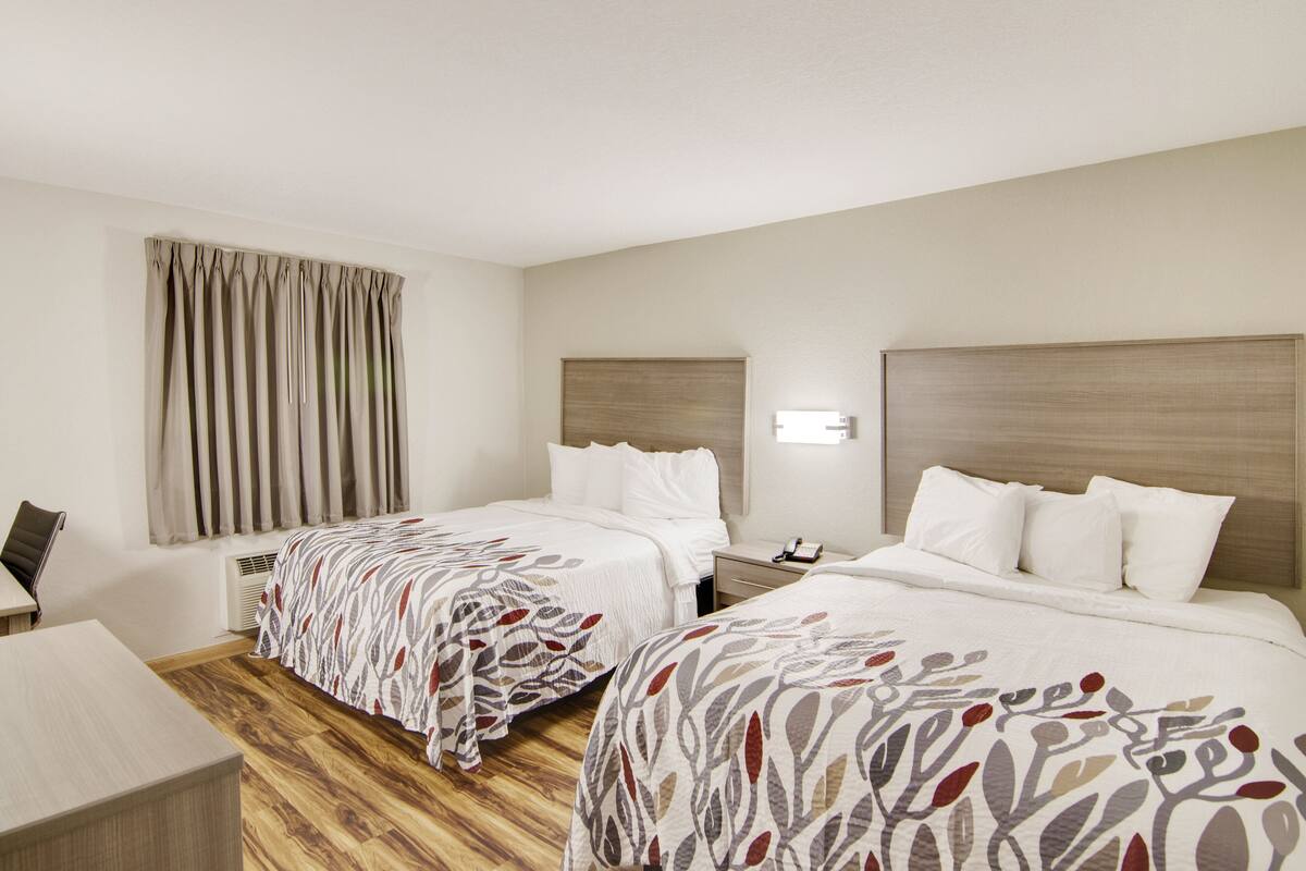 Habitación de hotel con dos camas, un escritorio y una ventana con cortinas.