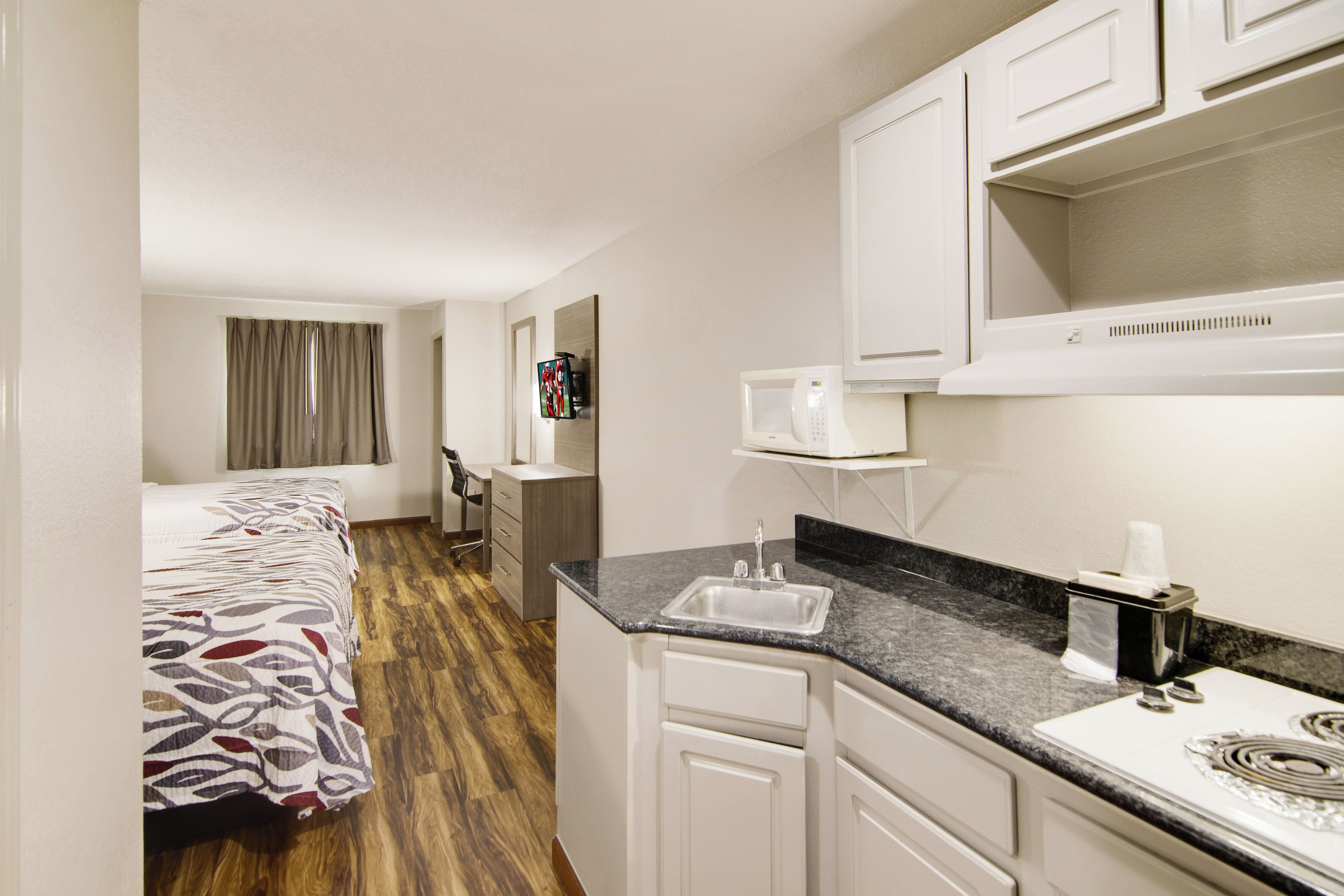 A hotel room with a bed, a desk, a kitchenette, and a bathroom.