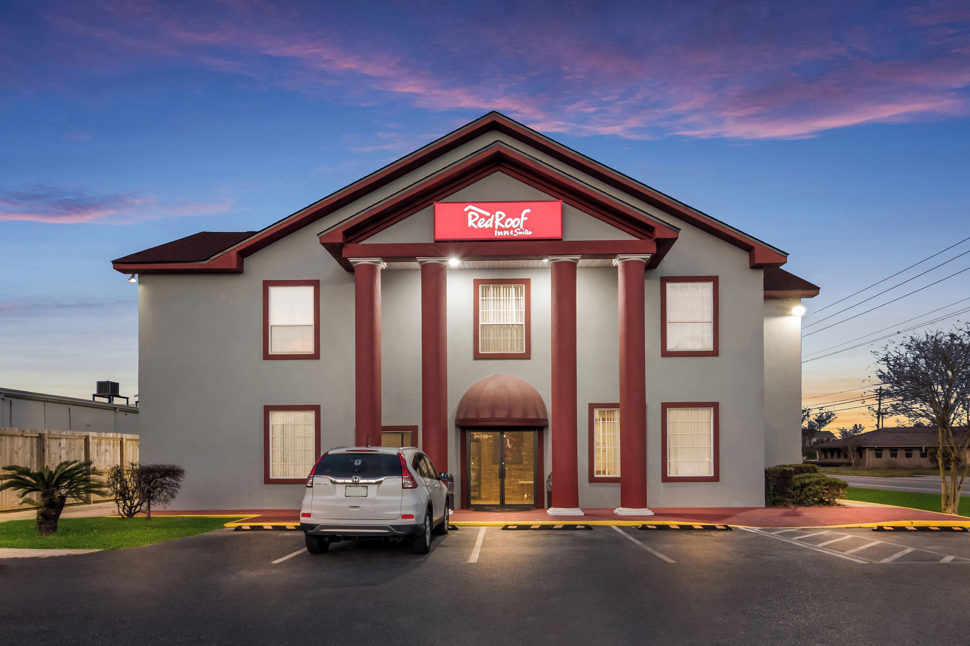 A hotel with a red and white facade, a central entrance with columns, and a parking lot in front.