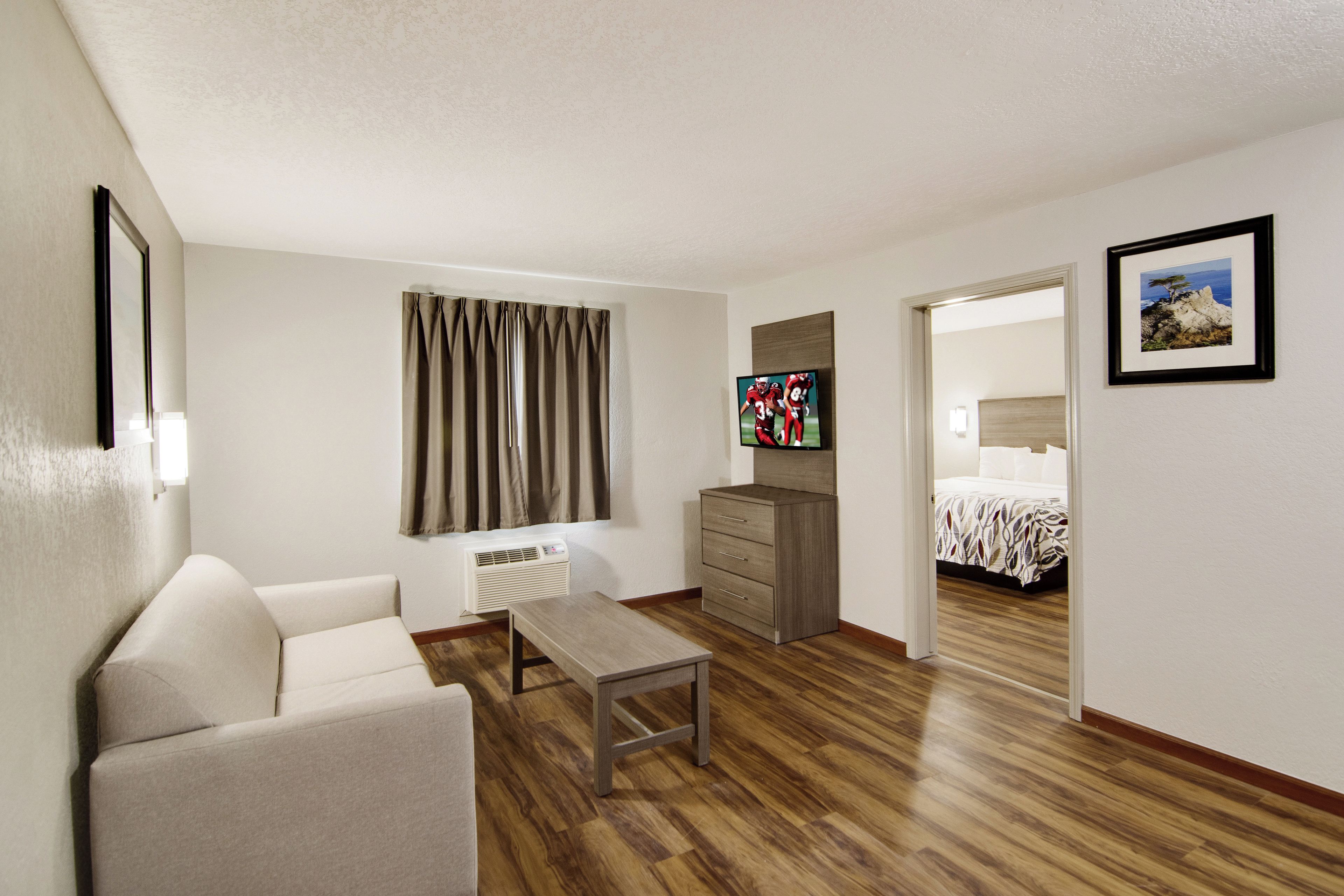Une chambre d’hôtel avec un plancher en bois, un canapé, une petite table, une télévision, un lit et un tableau au mur.