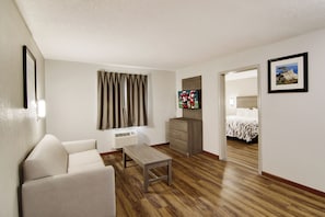 Een hotelkamer met een houten vloer, een bank, een kleine tafel, een televisie, een bed en een schilderij aan de muur.