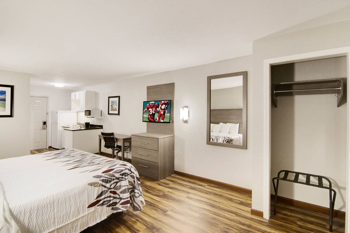Een hotelkamer met een bed, bureau, stoel, televisie, spiegel en kledingkast.