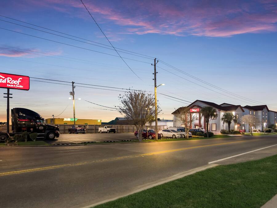 A Red Roof Inn & Suites with a parking lot, a building with a red awning, and a clear sky.