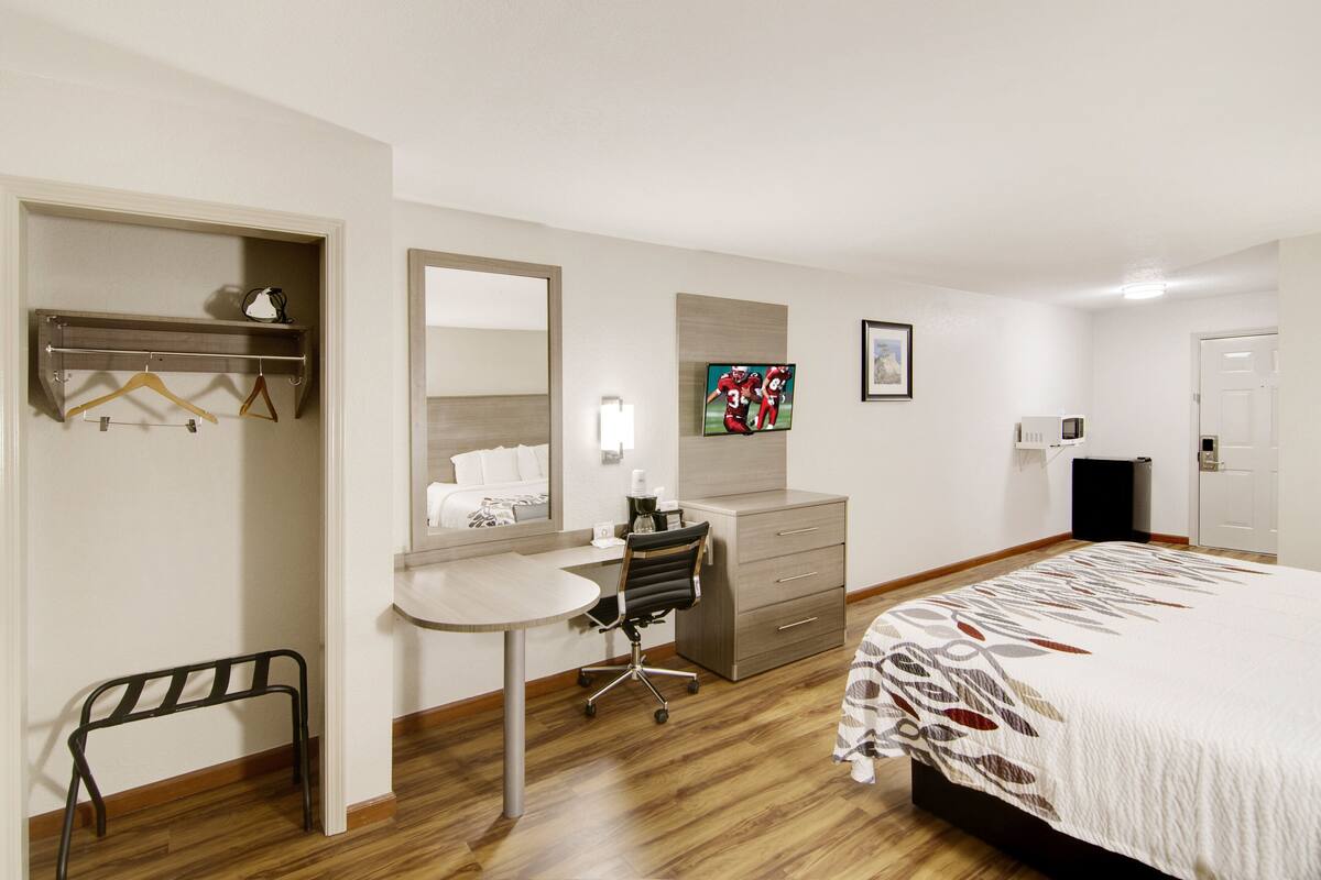 Een hotelkamer met een bed, een bureau, een stoel, een kledingkast en een spiegel.