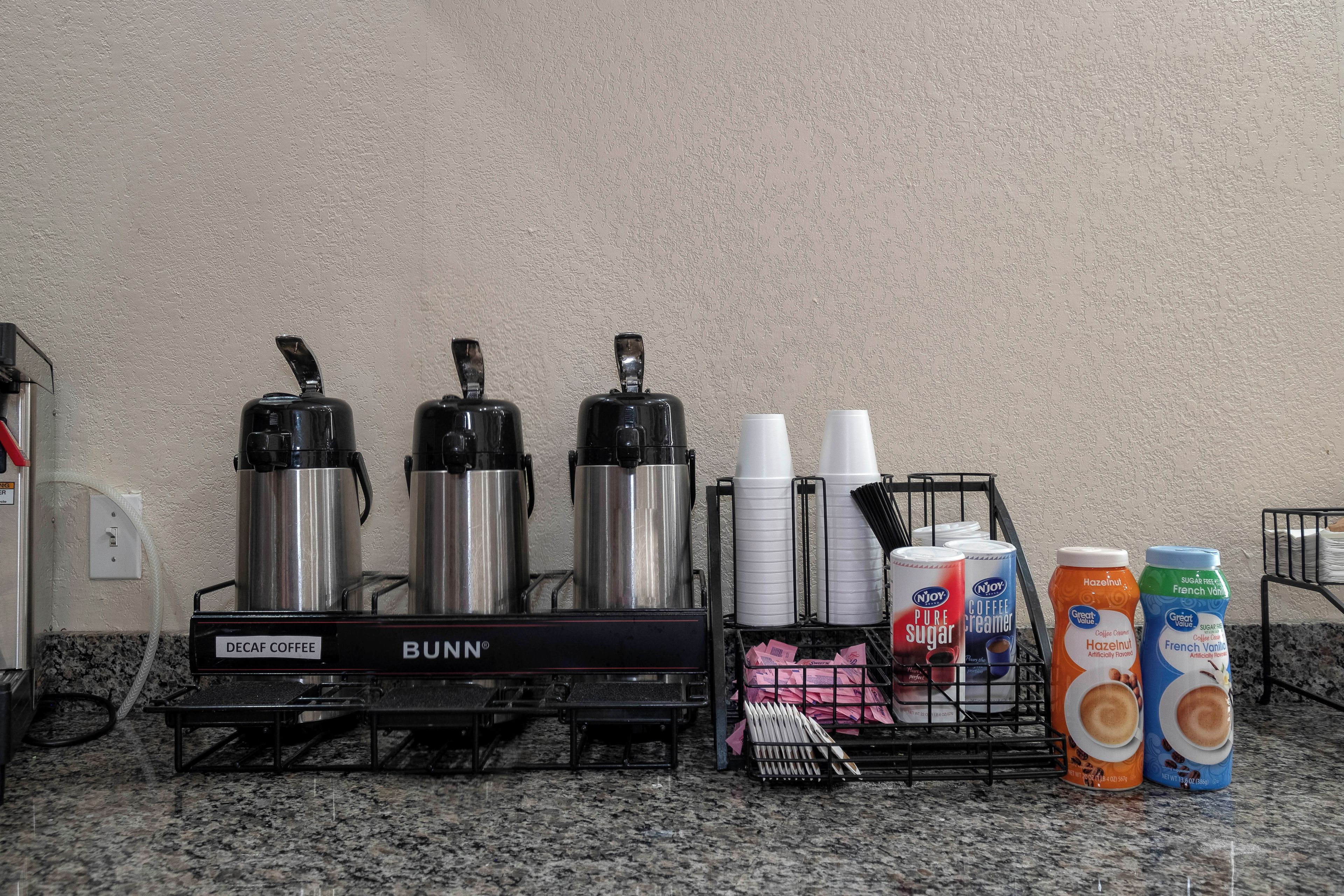 Una estación de café con máquinas de café Bunn, vasos desechables y leche vaporizada.