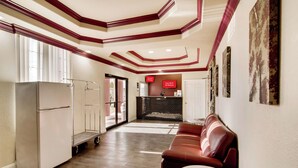 A hotel lobby with a modern design, featuring a wooden floor, a red leather sofa, a white coffee table, and a kitchenette area. - Red Roof Inn & Suites Pensacola - NAS Corry (Pensacola)
