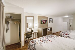 Une chambre d’hôtel comprenant un lit, un bureau avec une chaise, un miroir, une télévision et une armoire.
