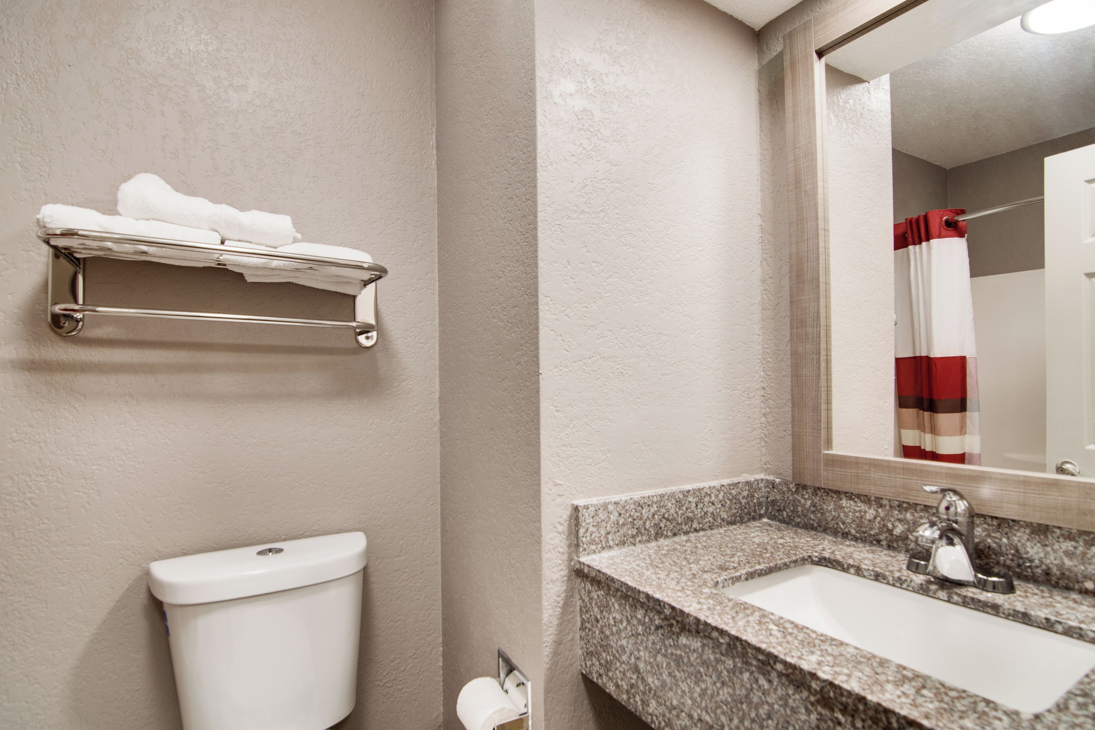 A bathroom with a toilet, a towel rack, a sink, and a mirror.