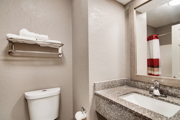 A bathroom with a toilet, a towel rack, a sink, and a mirror.