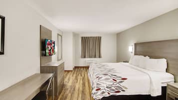Habitación de hotel con cama, escritorio, televisión y ventana con cortinas.