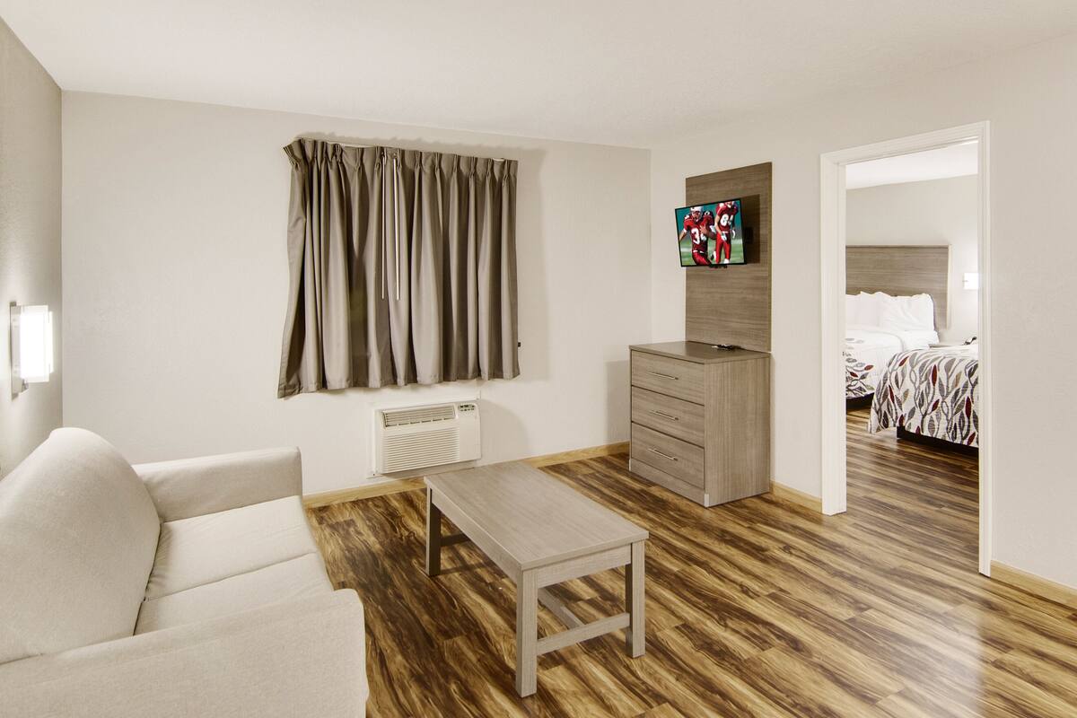 Een moderne hotelkamer met een houten vloer, een bank, een klein tafeltje, een aan de muur bevestigde televisie en een bed met een bedsprei met een patroon.