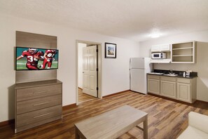 Un espacio habitable compacto con kitchenette, un televisor de pantalla plana montado en la pared, un banco de madera y una puerta que conduce a otra habitación.