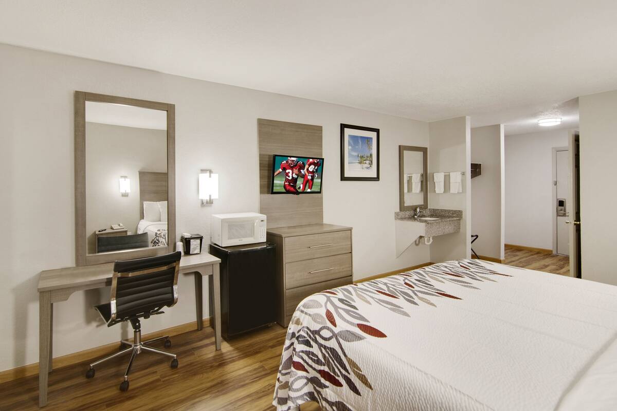 Een hotelkamer met een bed, bureau, stoel, magnetron en televisie.