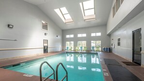 An indoor swimming pool with clear water, a diving board, and a view of the outdoors through large windows. - Red Roof Inn & Suites Pensacola - NAS Corry (Pensacola)
