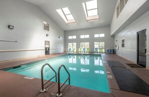 Une piscine intérieure à l’eau claire, dotée d’un plongeoir et offrant une vue sur l’extérieur grâce à de grandes fenêtres.