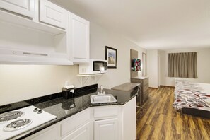 Une chambre d’hôtel compacte comprenant un coin cuisine, un lit avec une literie à motifs, un téléviseur à écran plat et une fenêtre avec des rideaux.