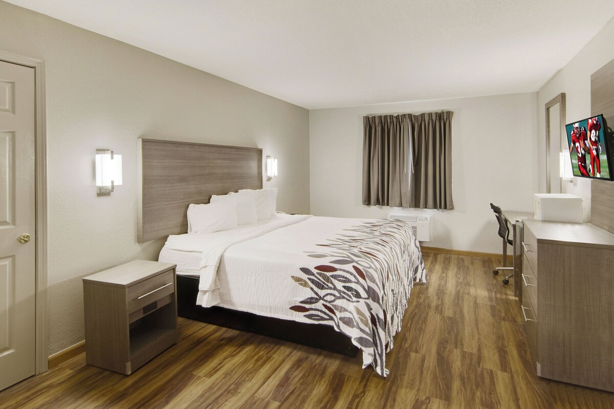 Une chambre d’hôtel comprenant un lit, des tables de chevet, un bureau, une chaise, un téléviseur et une fenêtre avec des rideaux.