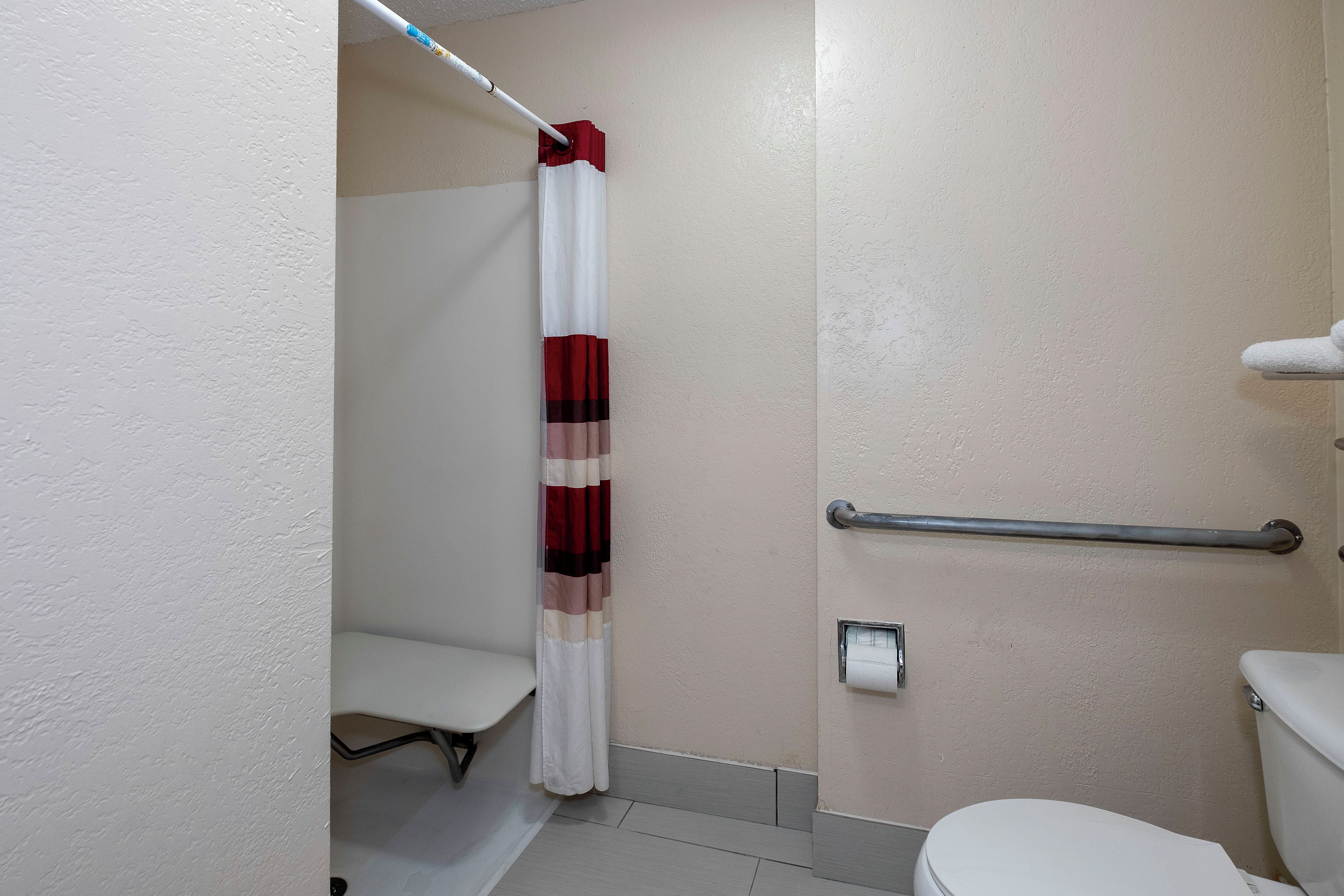 A bathroom with a white toilet, a shower curtain, a grab bar, and a towel rack.