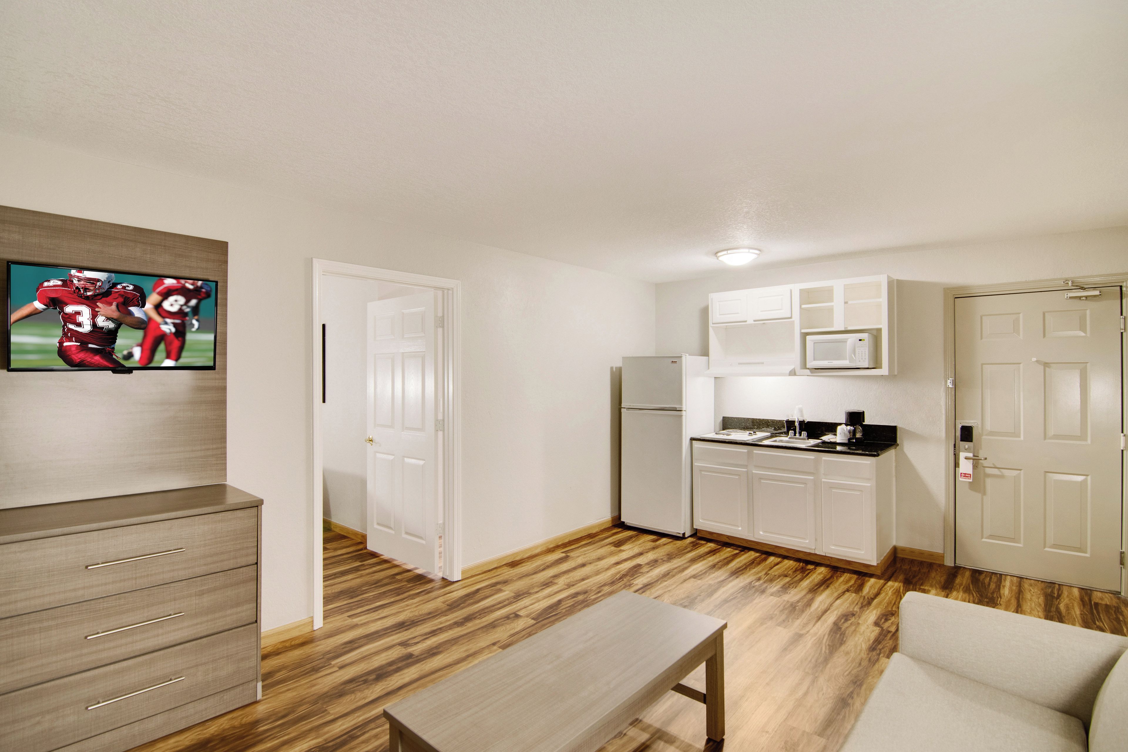 A compact living space with a kitchenette, a dining area, and a television mounted on the wall.