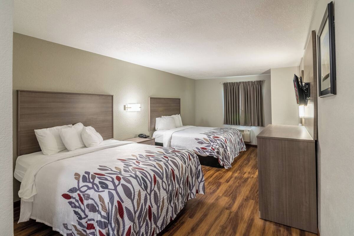 Een hotelkamer met twee bedden, een houten vloer, een bureau en een aan de muur bevestigde televisie.