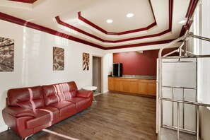 Un salon moderne avec un canapé en cuir rouge, des meubles en bois et un coin cuisine doté d’un réfrigérateur en acier inoxydable.