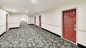 Een hotelgang met een kamerjas patroon, witte muren en rode deuren.