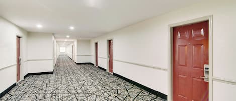 A hotel corridor with patterned carpet, white walls, and red doors.