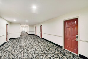 A hotel corridor with patterned carpet, white walls, and red doors.