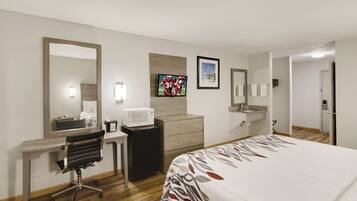 Una habitación de hotel con cama, escritorio, silla, microondas y televisión.