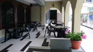 A restaurant with outdoor seating, including tables and chairs, and a potted plant with pink flowers. - Hotel Olimpico Quevedo (Quevedo)