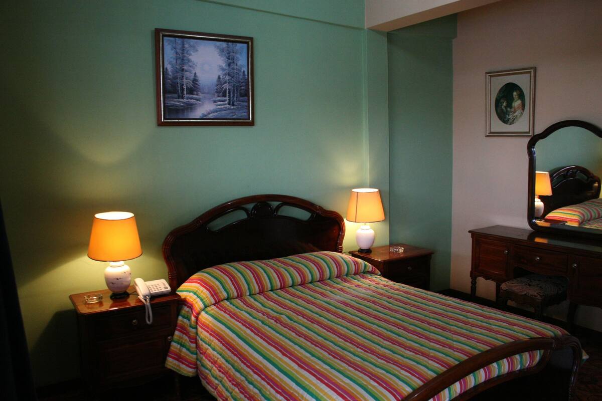 A bedroom with a bed, two bedside lamps, a nightstand with a phone, a dresser, and a mirror.