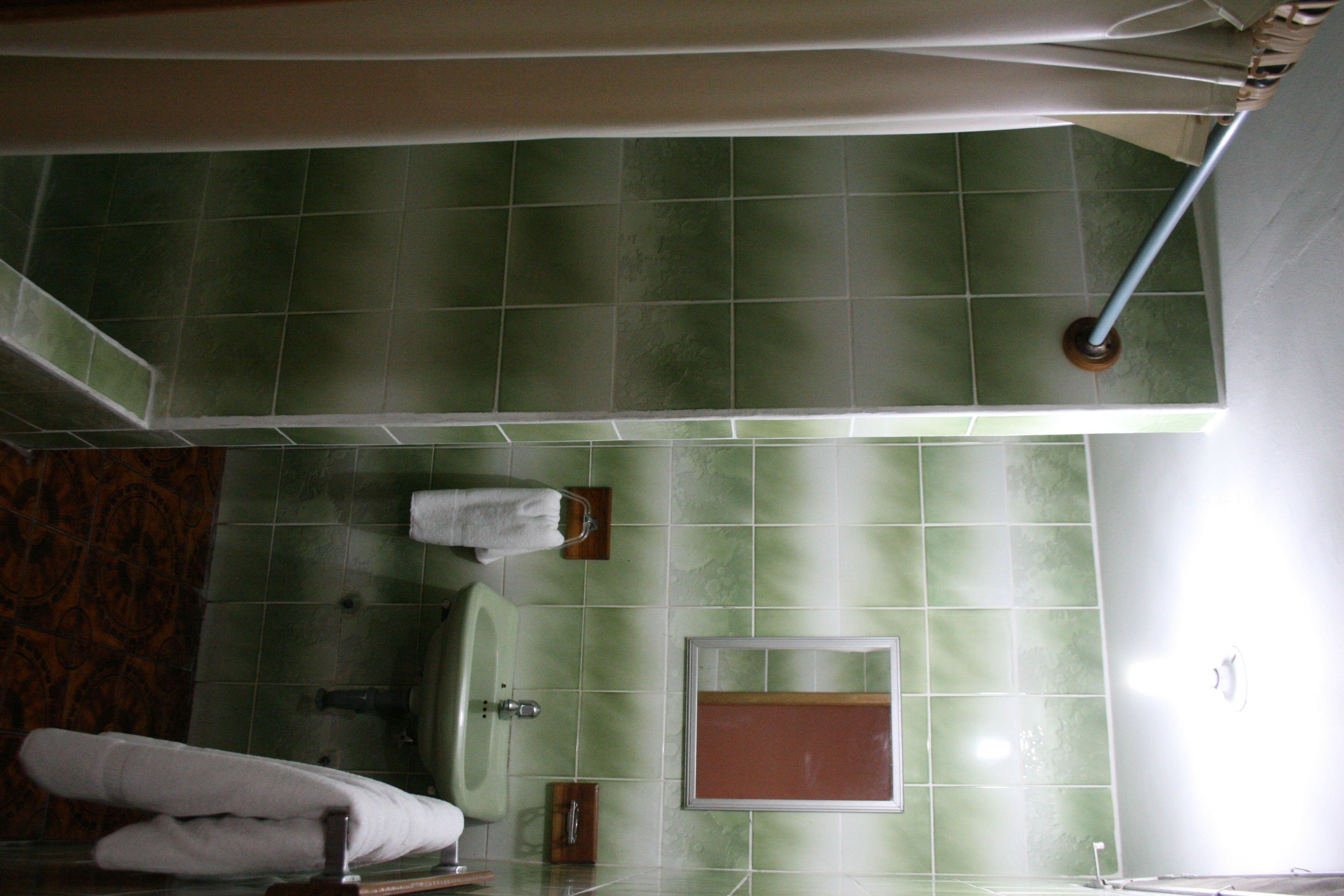 A bathroom with green tiles, a sink, a mirror, and a towel rack.
