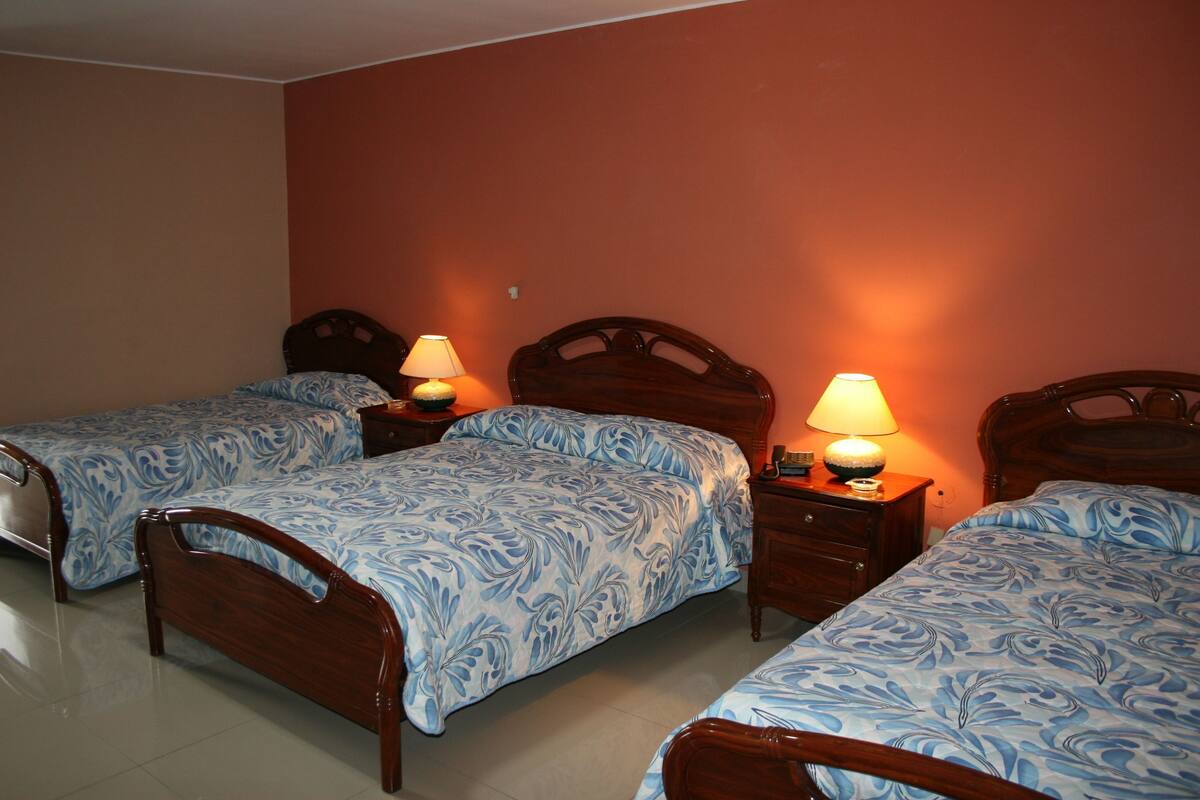 A bedroom with two single beds, wooden headboards, bedside tables with lamps, and a tiled floor.