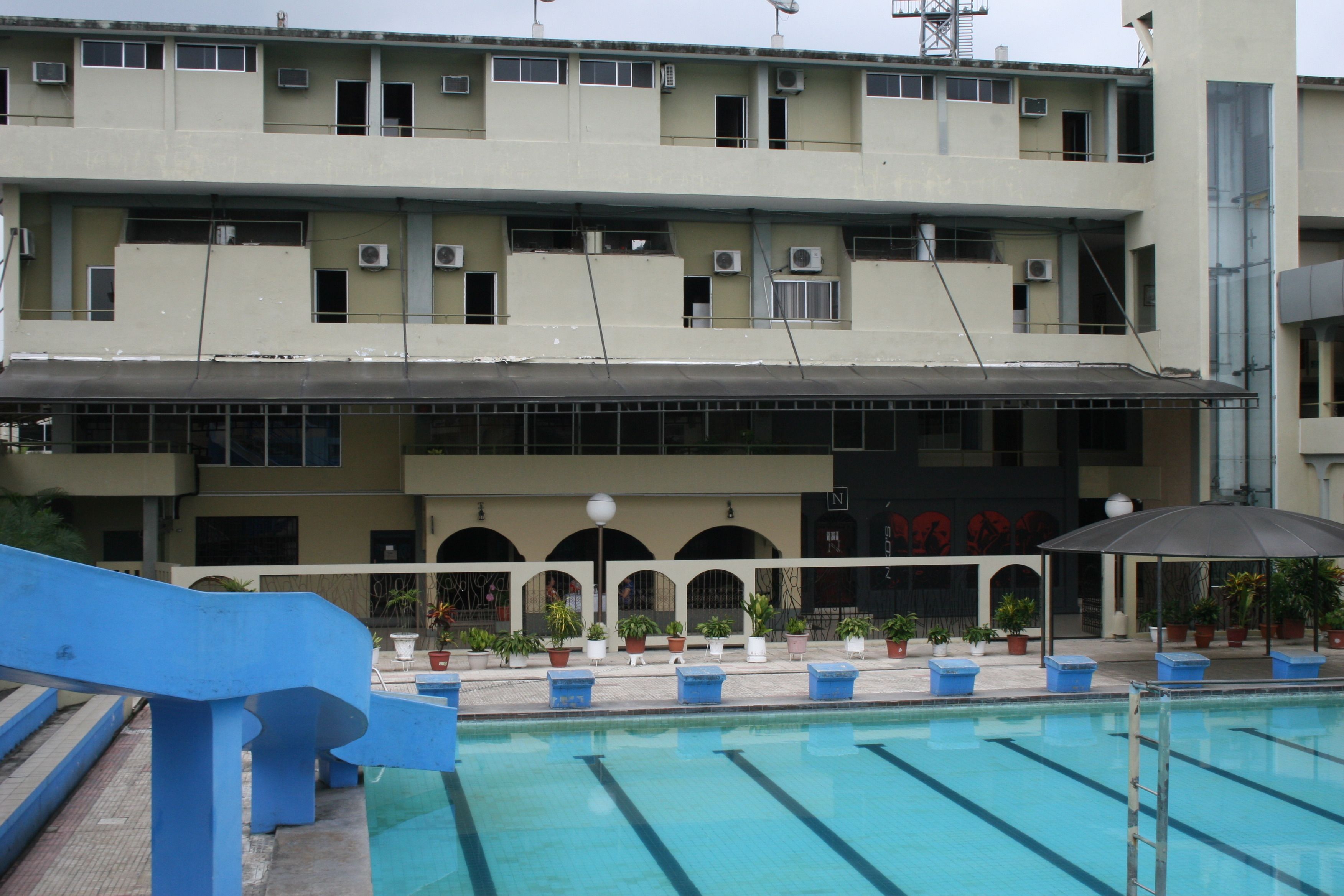 A building with a swimming pool, multiple balconies, and potted plants.