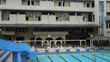 A building with a swimming pool, multiple balconies, and potted plants.