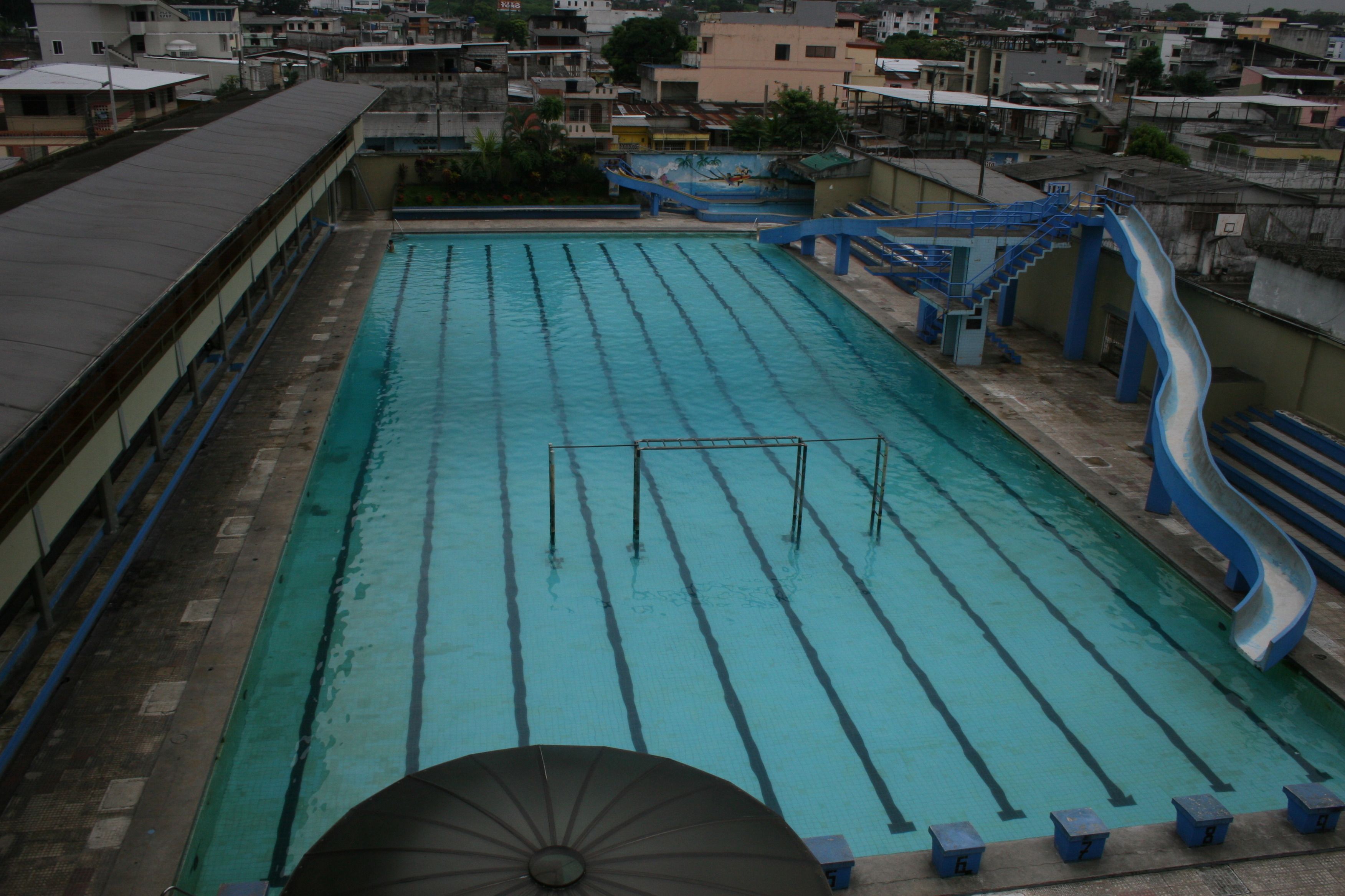 Una piscina con carriles de natación, un tobogán y una sombrilla.