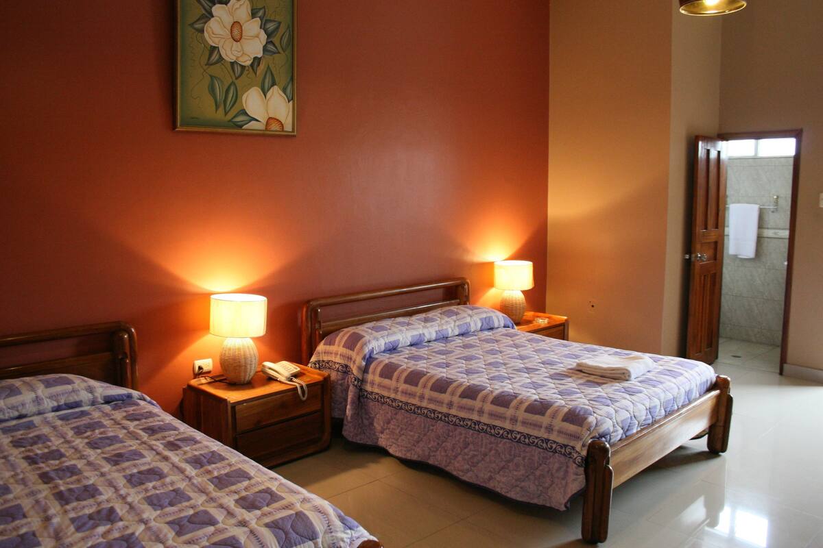 A hotel room with two beds, a painting on the wall, and a bathroom visible through an open door.