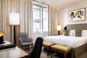 A hotel room with a bed, two bedside tables, a desk, a chair, and a window with curtains. - Le Tsuba Hotel (Paris)