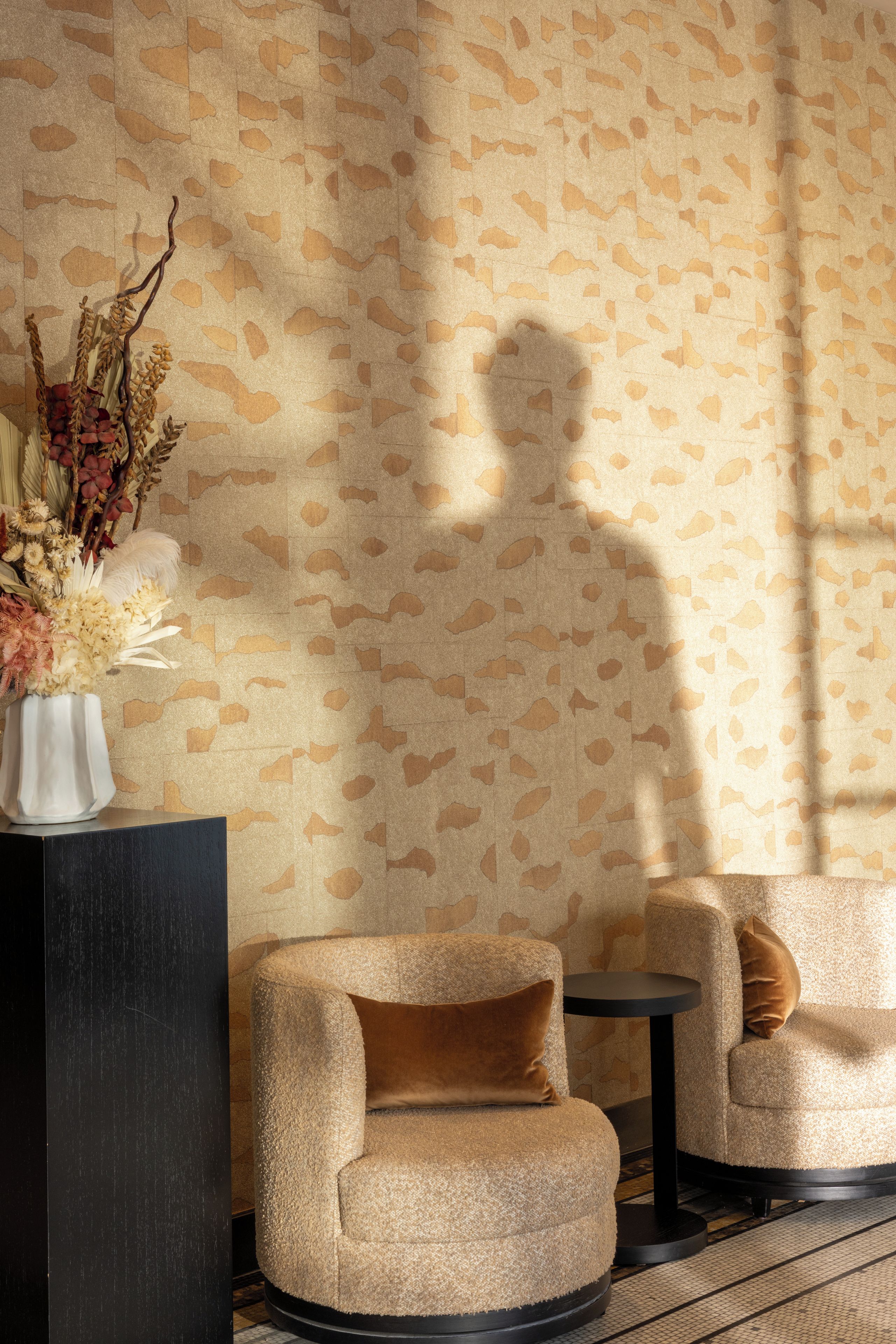 A room with a patterned wallpaper, a vase with dried flowers, and two armchairs with a round table.